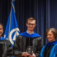 Provost Mili takes picture with 2 males on stage